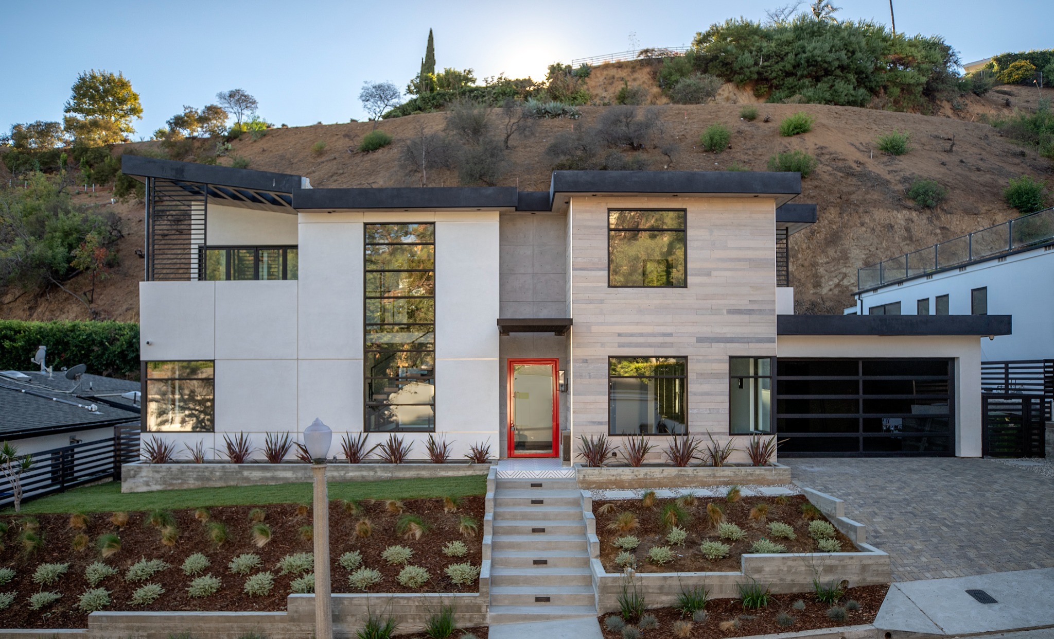 Sunset Plaza hillside residence with concrete, wood cladding, black-framed glazing, and a red entry door